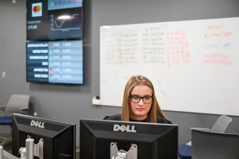 UTC Business Analytics student looking at a computer with stock data on a screen in the background